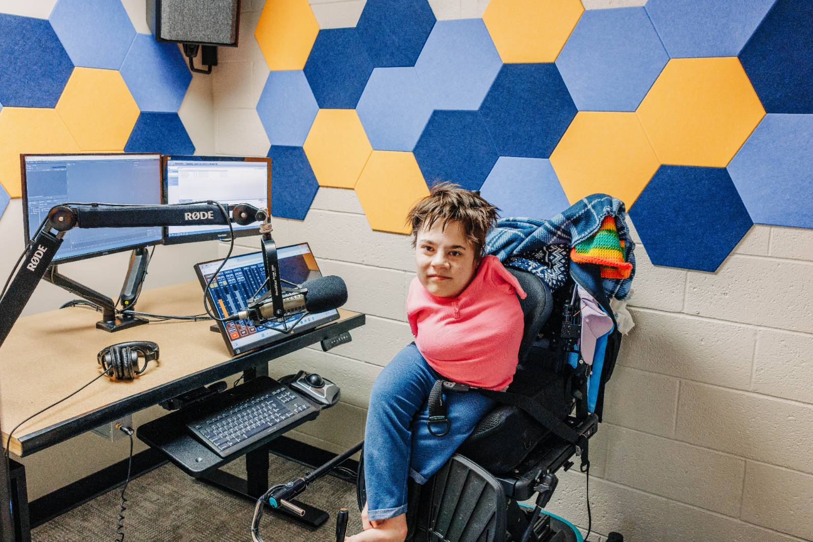 A disabled student with bilateral upper limb difference sits in front of audio recording equipment