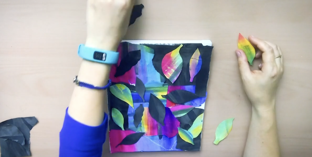 hands applying colorful paper leaf shapes to a small paper art piece
