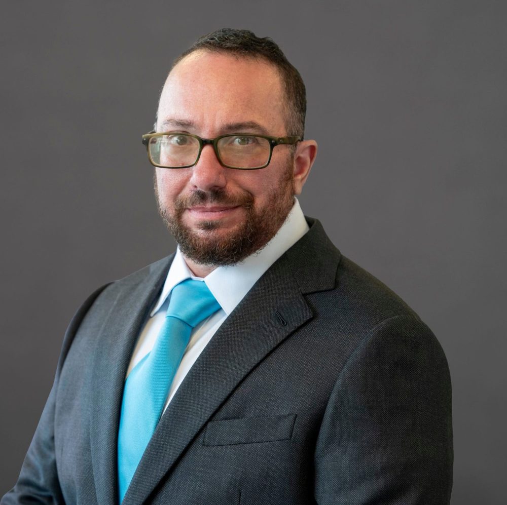 A trans man with a beard, glasses, brown short hair