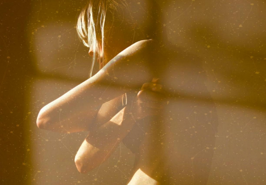 A potion of the film poster from the documentary This is Endometriosis, a grainy cepia colored image showing a contorted woman standing naked with shadows across it