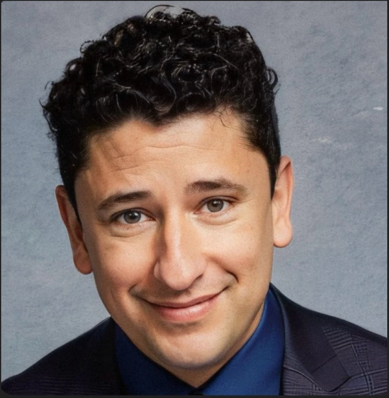 a man with short black curly hair a dimpled smile wearing a suit